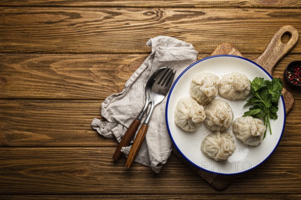 Khinkali, traditional dish of Georgian Caucasian cuisine, dumplings filled with ground meat on white plate with herbs on wooden rustic background table top view space for text