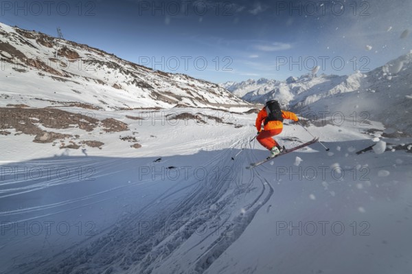 An athlete male skier jumps from a snow-covered slope against the backdrop of a mountain landscape of snow-covered mountains on a sunny day. The concept of winter sports