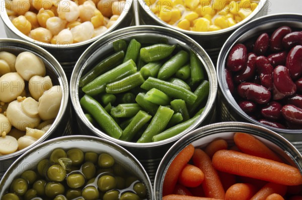 Canned vegetables in opened tin cans on kitchen table. Non-perishable long shelf life foods background