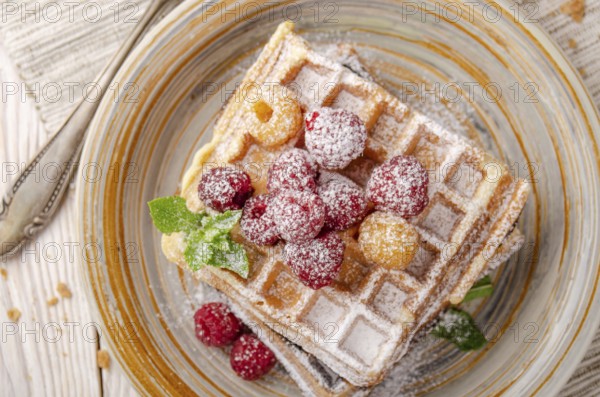 Flat lay view at Belgian waffles served with raspberries and mint leaf dusted with powdered sugar