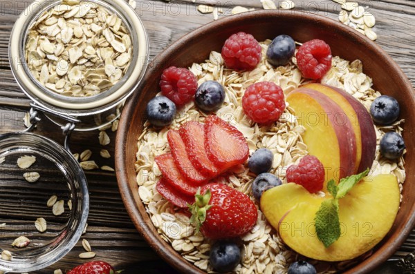 Flat lay of fruit healthy muesli with peaches strawberry almonds and blackberry in clay dish on wooden kitchen table