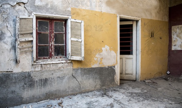 Backyard of a deserted abandoned house with a broken closed window and door and with yellow cracked wall