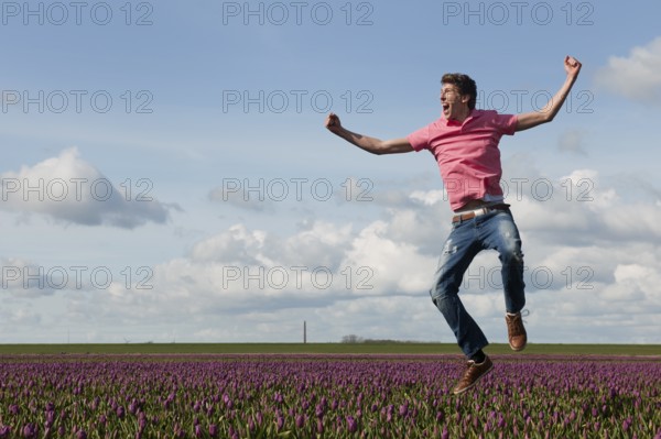 Young man is jumping above the typical dutch tulips