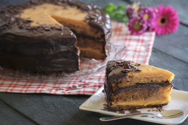 Tasty piece of cake with a Brigadeiro filling made with condensed milk and chocolate, with the whole cake in the background, on a rustic back table