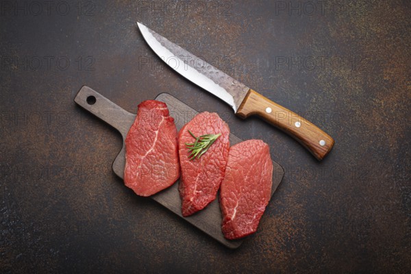 Three raw uncooked meat beef top sirloin steaks on wooden cutting board with rosemary on wooden cutting board with knife on dark rustic background from above, preparing meal with meat, food photography, food photography