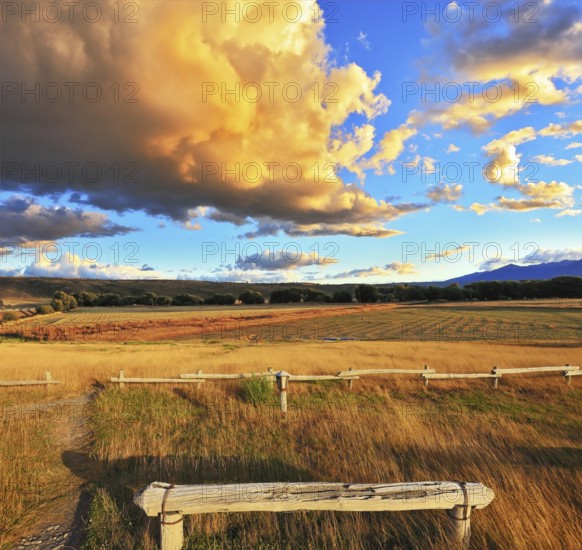 The huge cloud lit yellow-orange rays of sunset. Cozy wooden bench by the side of the road in Argentina
