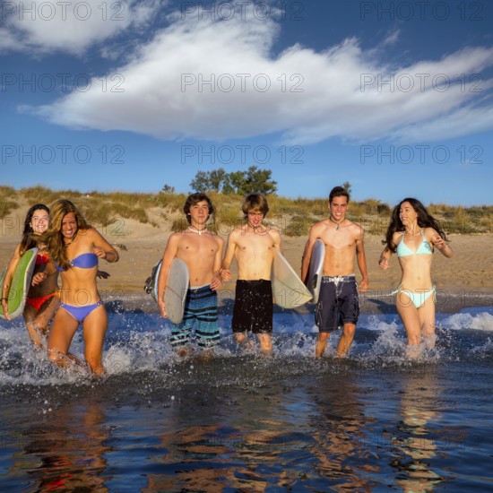 Teen surfers boys and girls group running happy to the beach splashing water