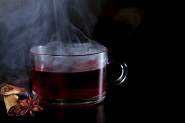 Steaming cup of hot tea with star anise and cinnamon stick isolated on black background and copy space