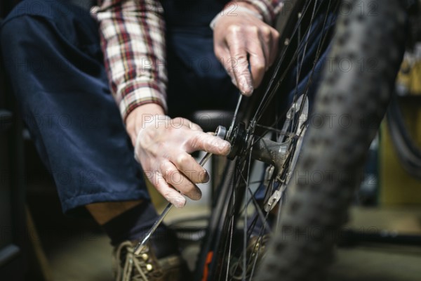 Male mechanic working in bicycle repair shop, mechanic repairing bike using special tool, wearing protective gloves. Young attractive serviceman fixing customer's bicycle wheel at his own workshop