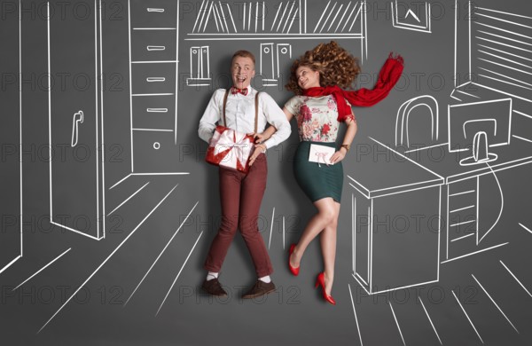 Happy valentines love story concept of an office romance. Young couple at work smiling at each other and exchanging gifts against chalk drawings office background
