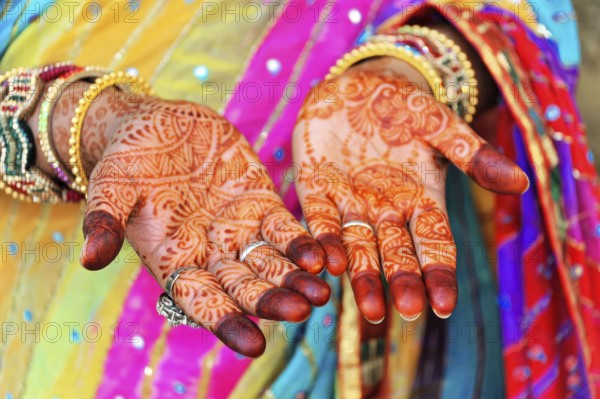 Close-up of painted hands with elaborate mehndi designs, accompanied by colourful robes, Rajasthan, North India, India, Asia