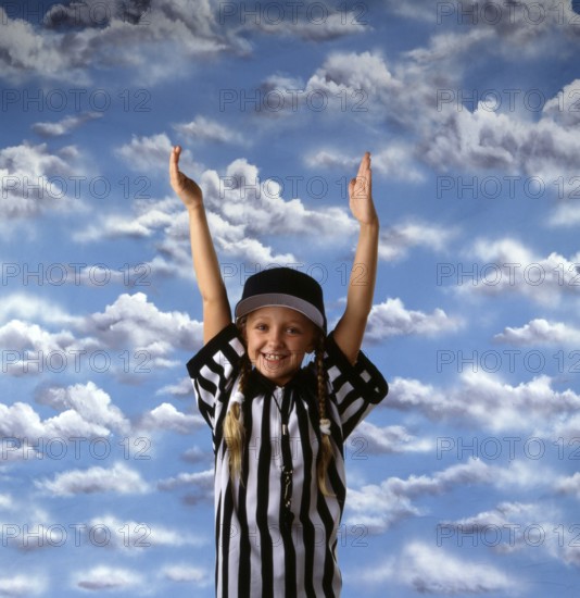 Smiling girl in referee outfit with hands raised against a vibrant sky, expressing joy and celebration