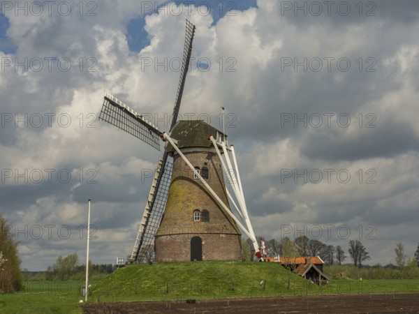 A historic windmill stands on a green meadow under a cloudy sky, Eibergen, Gelderland, Netherlands