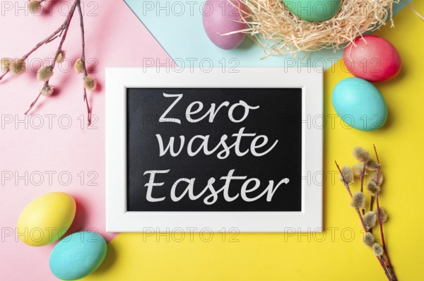 Zero waste Easter concept. Colorful eggs and pussy willow branches on bright colorful background and chalkboard with Zero waste Easter letters. Top down view or flat lay