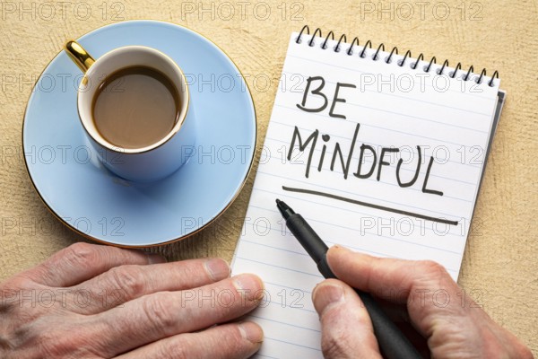 Be mindful - man hand writing a note with a black marker in a spiral notebook
