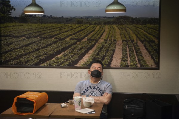 06.03.2020, Singapore, Republic of Singapore, Asia, A man sleeps in a Starbucks cafe and wears a mask to protect himself from infection with the pandemic coronavirus, Asia