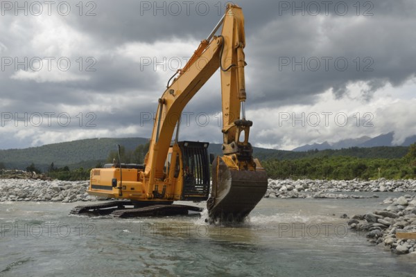 10 ton digger shifting shingle to deepen the channel in a flowing river, Westland, New Zealand, Oceania
