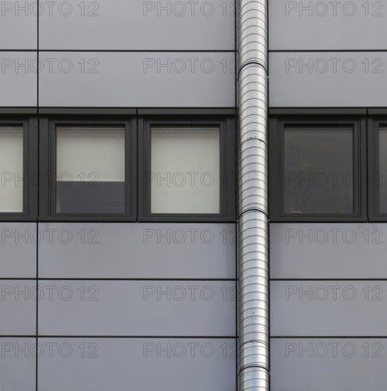 Grey cladding panels on an industrial building with a row of back window frames and a silver pipe running up the wall