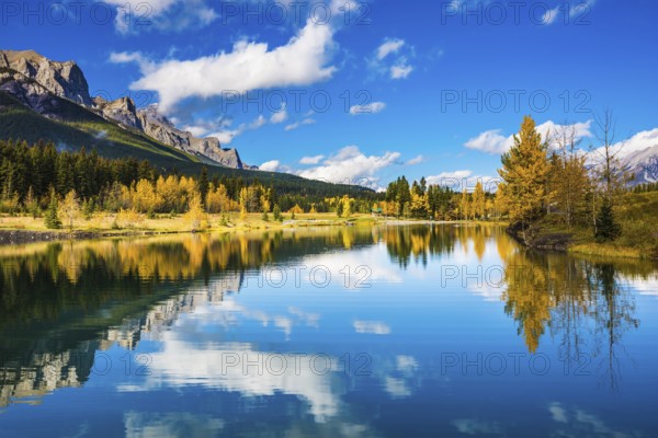Concept hiking. Canmore, near Banff. Jagged mountains and red-orange trees are reflected in the smooth water of the lake
