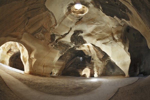 Israel National Park. Bell caves of Beit Guvrin. Picturesque clay arches illuminated by the sun from the hole at the top and side entrances