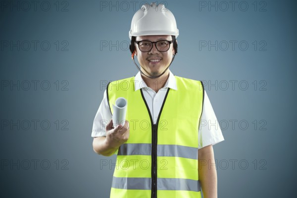 Porträt eines zuversichtlichen asiatischen jungen Ingenieur mit schützenden harten Hut und halten Papier blauabdruck