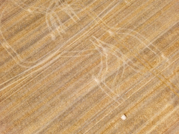Striking tracks and patterns from a tractor on a dry agricultural field with straw bales, aerial view from Germany