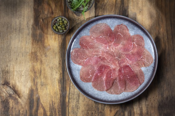 Food, Marbled beef for carpaccio with ingredients arugula and capers on gray plate, wooden background, top view