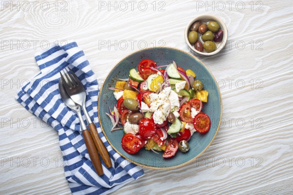 Greek fresh healthy colorful salad with feta cheese, vegetables, olives in blue ceramic bowl on rustic white wooden background top view, Mediterranean diet, traditional cuisine of Greece, food photography, food photography