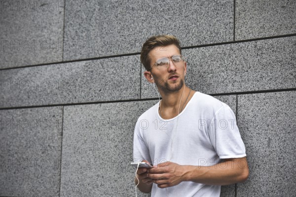 People, technology, travel and tourism, man with earphones, smartphone on city street and listening to music over gray wall background