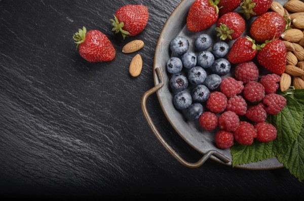 Tray with ripe organic bilberry raspberry strawberry and almonds set on slate closeup