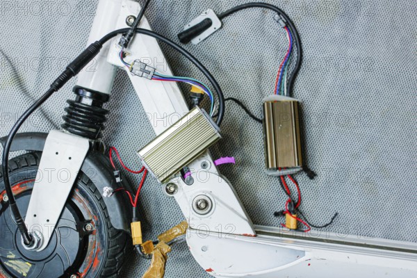Electric scooter with exposed components and wiring, showcasing mechanical details on a grey surface