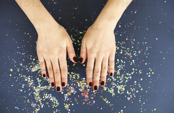 Top view of crop anonymous female with bright manicure over dark blurred background with colorful confetti