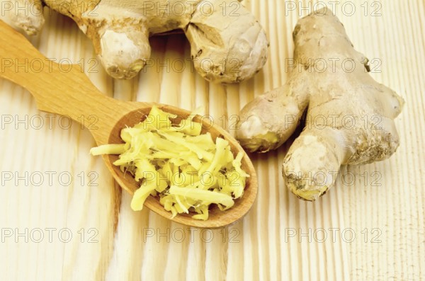Wooden spoon with grated ginger, ginger root against a wooden board