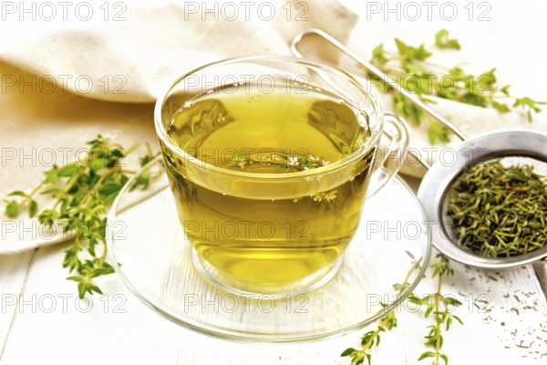Herbal tea in a glass cup of thyme, a metal strainer with dry leaves, a linen napkin on the background of a light wooden board
