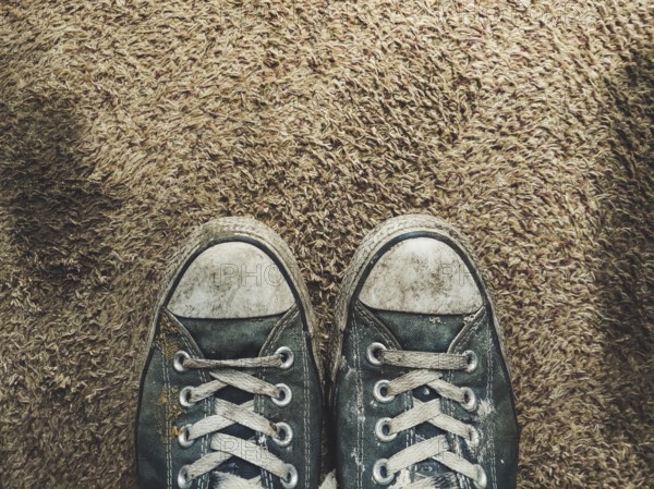 Pair of worn out black sneakers on brown carpet