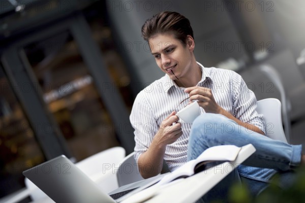 Handsome caucasian young man working on laptop and smiling while enjoying coffee in cafe