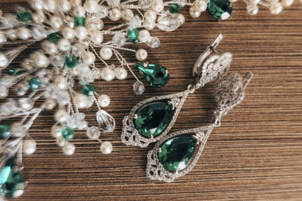 Earrings with a large emerald and an ornament of white beads on a brown background with a rough texture.