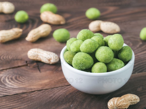 Peanut snack for beer, wine, party bar. Salted peanuts in green vasabi glaze on brown wooden table. Copy space