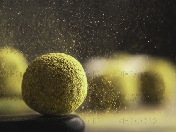 Homemade truffles candy with matcha tea powder in green tea dust cloud over dark background. Copy space right for text or design, banner. Shallow depth of field