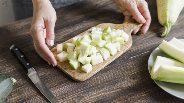 Zucchini harvest. Woman slices zucchini cubes for freezing on wooden table. Farm organic zucchini harvesting