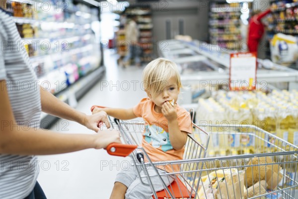 Budva, Montenegro - 17 march 2021: A child sits in a trolley in a supermarket and eats a bun