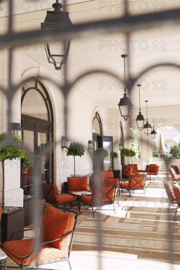 View through the wrought-iron lattice onto the hotel terrace with soft chairs and tables.
