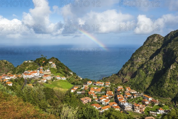 View from the Miradouro de Pastel over the small coastal village of Boaventura with its orange roofs to the Atlantic Ocean, with a rainbow and clouds in the sky, Madeira, Portugal, Europe