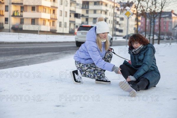 A woman, who was out walking her dog, tries to help a person who fell over in the snow. The girl fell and bruised her leg. She needs help to get up