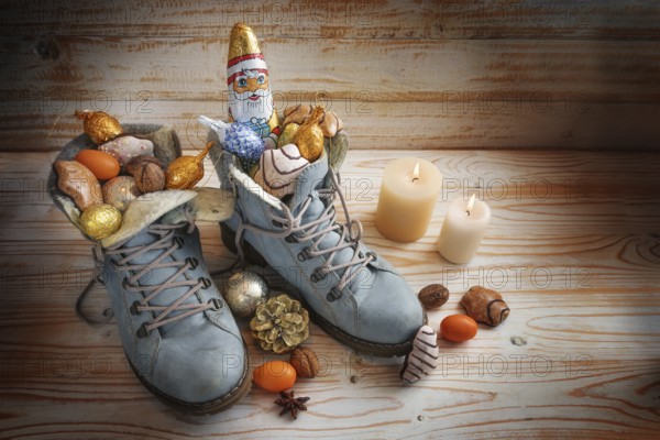 Boots filled with sweets, chocolate Santa and Christmas decoration on a wooden background with candles, tradition on German Nikolaus Tag meaning Nicholas day, copy space