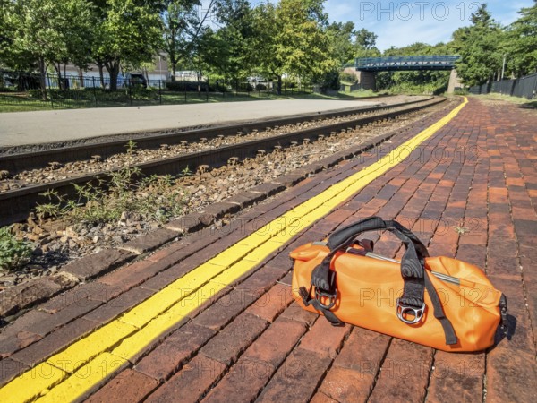 Waiting for a train concept - a bright orange duffel on a station platform behind yellow line