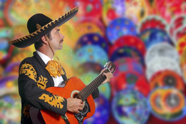 Charro Mariachi playing guitar over colorful blur handcrafts background