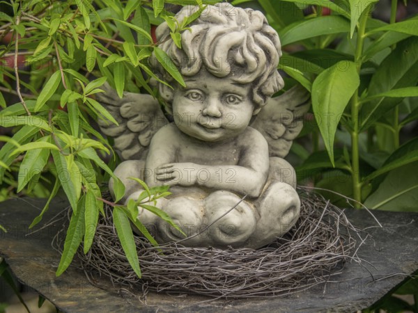 Angel statue in a nest of twigs, surrounded by green leaves in the garden, borken, münsterland, germany