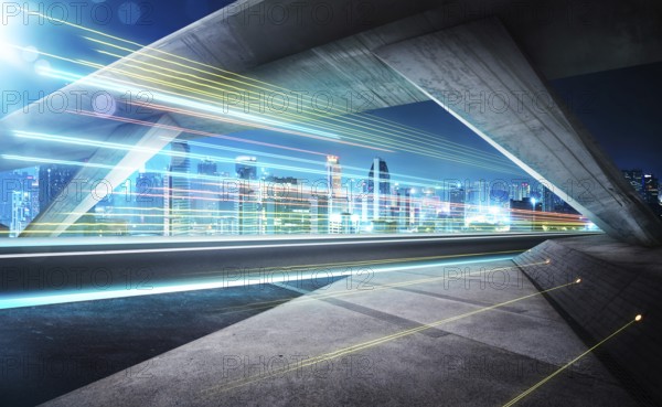 Empty asphalt road under the bridge during the night with light trails and beautiful city skyline background