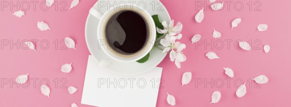 Creative flat lay concept top view of coffee cup and white apple tree flowers petals on pastel pink background with postcard mock up and copy space in minimal style template for text. Long wide banner